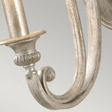 Close-up of an ornate, metallic arm featuring a scroll design and a weathered Silver Sand finish, part of the Abbey 1 Light Wall Light collection, set against a light gray background.