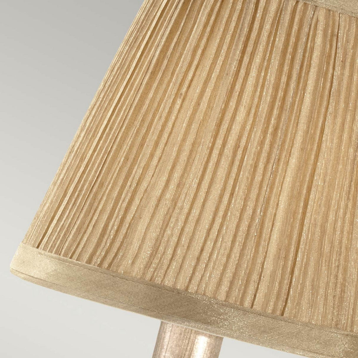 A close-up of the Abbey 1 Light Wall Light in Silver Sand showcases its beige pleated lampshade against a light gray background. The fabric's delicate texture and vertical folds give it an elegant look, enhanced by a smooth trim along the edge.