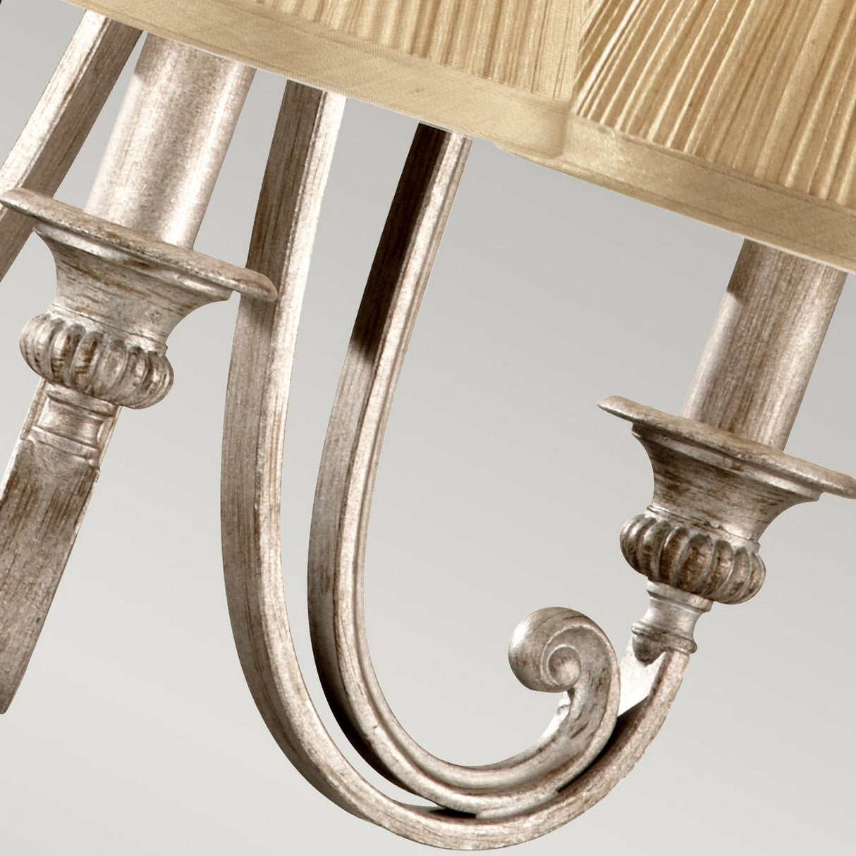 Close-up of the Abbey 3 Light Chandelier in Silver Sand, showcasing its intricate detailing and classic style with a gold pleated shade and elegantly curved decorative silver metal arm, set against a neutral background.