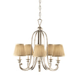 The Abbey 5 Light Chandelier - Silver Sand features a captivating finish and timeless design. With five lamps adorned with elegant beige fabric shades, it is gracefully suspended by a chain to add sophistication to any space.