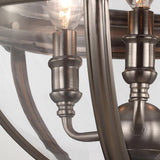 A close-up of the Adams 3 Light Chandelier in antique nickel features clear glass shades and intricate metal detailing with lit bulbs inside. It boasts a brushed silver finish, providing Victorian-inspired lighting with a modern and elegant design that emphasizes classic craftsmanship.