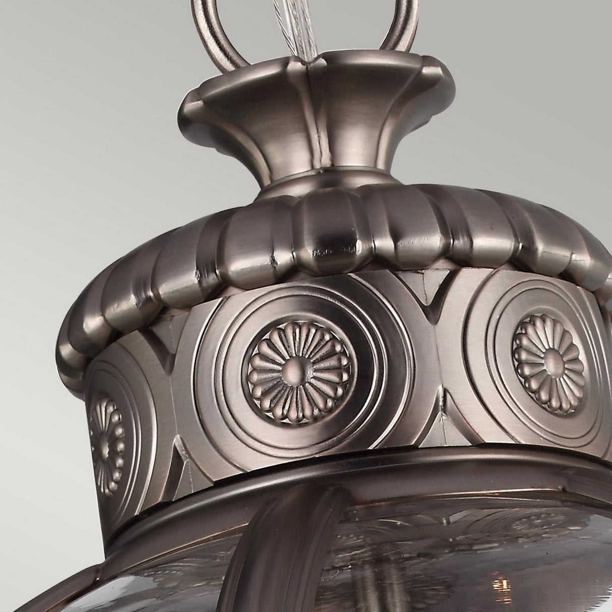 A close-up view of the Adams 3 Light Chandelier in Antique Nickel reveals its ornate metallic design, featuring intricate circular patterns and a smooth brushed finish. The classic craftsmanship showcases embossed floral details reminiscent of Victorian-inspired lighting, all set against a neutral background.