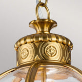 A detailed view of the Adams 3 Light Chandelier in a burnished brass finish, showcasing its ornate circular and floral motifs that echo Victorian lighting design. The fixture is adorned with clear glass panels and elegant metalwork.