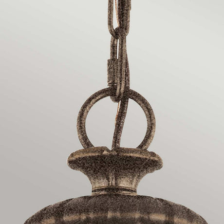 A close-up of the Adams 3 Light Chandelier - British Bronze, featuring a metallic hanging light fixture with a vintage charm and weathered, textured surface. The focus is on the chain and circular connecting ring at the top, which echoes its British bronze finish against a plain gray background.