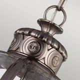 A detailed view of the Adams 4 Light Chandelier - Antique Nickel highlights its Victorian-inspired elegance, featuring intricate circular patterns and a metallic finish. The glass element harmonizes beautifully with the Antique Nickel chain against a simple background.