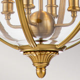 Close-up of the Adams 4 Light Chandelier in burnished brass. The design showcases elegant, curved brass arms with a reflective glass enclosure and intricate detailing at the base. This Victorian-inspired lighting piece adds a vintage and sophisticated touch to luxury home decor.