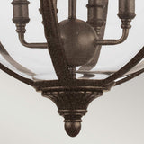 A close-up of the Adams 4 Light Chandelier in British Bronze highlights its vintage-style charm with a curved metal frame and clear glass cover. This chandelier boasts the intricate Victorian Era design details, featuring a central spherical hub with extending bulb sockets, all set against a neutral-toned background.