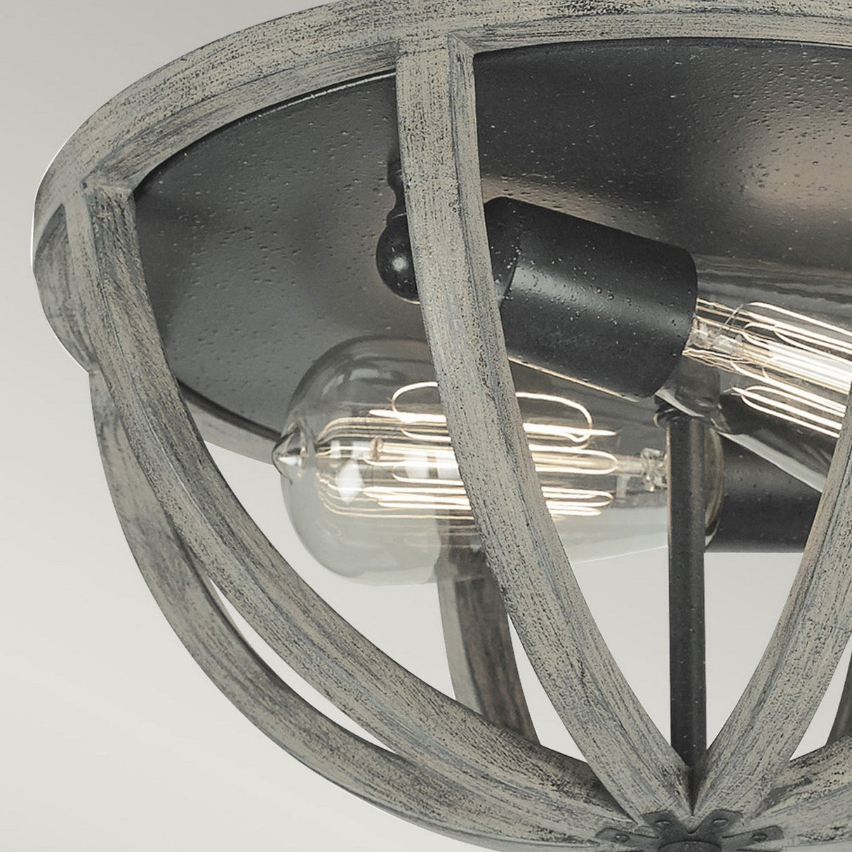A close-up of the Allier 2 Light Flush showcases its rustic design with exposed Edison bulbs. The orb-shaped fixture, constructed from weathered oak wood and accented with antique forged iron, emphasizes the glowing filaments against a neutral backdrop.
