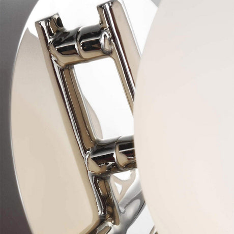 Close-up of a modern lamp showcasing geometric shapes and a chrome-like aesthetic. The Apollo 1 Light Wall Light - Polished Nickel displays intersecting circular and rectangular elements, enhanced with white opal etched glass, forming an intricate and artistic composition.