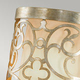 Close-up of an Arabesque 1 Light Wall Light in a silver leaf patina frame. The pattern showcases swirling and floral designs, reminiscent of laser-cut scrollwork, and the lamp emits a warm, soft glow against a neutral background.