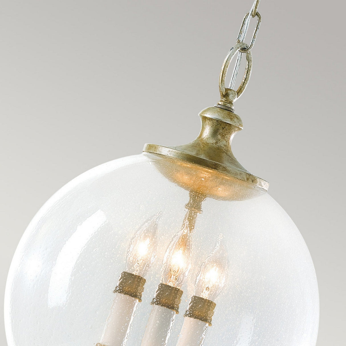 Close-up of the elegant Argento 3 Light Chandelier in oxidized silver leaf, with a spherical hand-blown bubble glass design and three candle-style bulbs inside. The fixture is complemented by a brass top and chain, set against a neutral background.