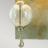 A close-up of the Argento 1 Light Wall Light - Oxidized Silver Leaf showcasing a vintage bubble glass orb with a small metallic teardrop ornament hanging below. The fixture is mounted on an oxidized silver leaf wall plate, adding character and charm to any space.