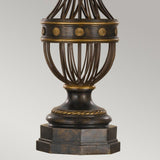 The Augustine 1 Light Table Lamp features an antique brown finish with vertical metal bars forming a graceful oval shape, ideal for transitional interiors. It stands on a detailed pedestal, with the bars connected by a horizontal band embellished with flower-like patterns. The lamp's classic bronze design is highlighted with gold accents, reminiscent of ornate decorative pieces.