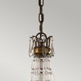 Introducing the Bellini 6 Light Chandelier, featuring cascading glass prisms and antique quartz crystals suspended from a dark chain. Its ornate metal crown, adorned with elongated crystal pendants, beautifully contrasts against a plain gray background. This luxurious piece comes in an exquisite Oxidized Bronze/British Bronze finish, epitomizing luxury lighting at its finest.