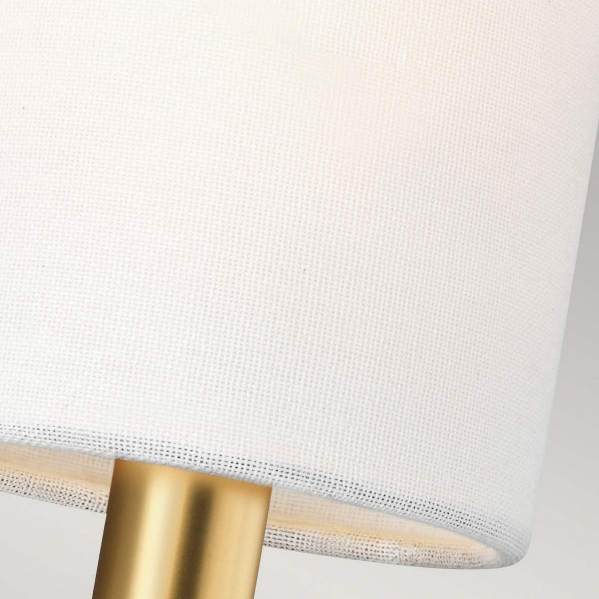 Close-up of the Brianna 2 Light Wall Light showcasing a white linen cylindrical shade paired with a burnished brass base. The image beautifully highlights the fabric's texture and the metal's smooth finish.