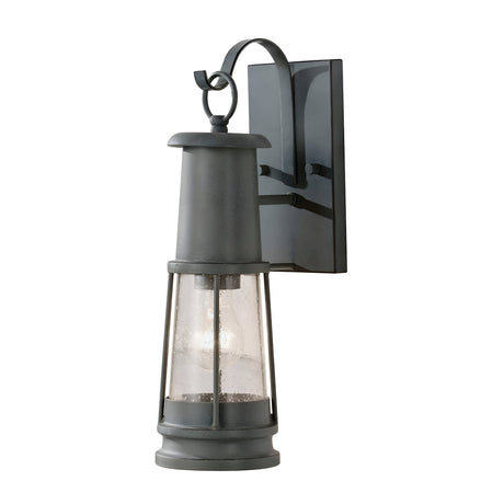 The Chelsea Harbor 1 Light Outdoor Wall Lantern in Storm Cloud offers a vintage aesthetic with its weathered finish. It highlights a rectangular backplate, a curved arm, and features a tapered glass enclosure decorated with droplets for an authentic retro appearance. Designed for wall mounting, this outdoor light enhances any exterior space beautifully.
