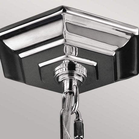 Close-up of the Corinne 3 Light Small Chandelier, showcasing its polished nickel finish. A metal cable and hook are affixed to the sleek, chrome square ceiling piece against a light gray background.