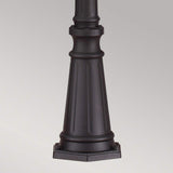 A detailed view of a black cylindrical pedestal with vertical grooves and a hexagonal base, reminiscent of the elegance captured by the Cotswold Lane 3 Light Large Post - Black, set against a plain gray background.