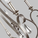 Close-up of the DeWitt 5 Light Chandelier - Silver, featuring elegant curved metal arms adorned with teardrop crystals against a gray background. Its antique, brushed finish enhances its classic French Provincial design.