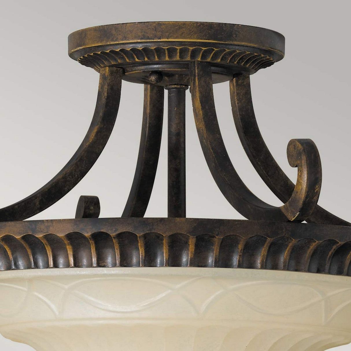 The Drawing-2 Room 2 Light Semi Flush in Walnut showcases an ornate ceiling light fixture with a bronze and walnut finish, featuring decorative scrollwork reminiscent of Edwardian design. It includes a frosted glass dome embellished with an elegant carved pattern.