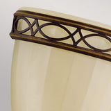 A close-up of the Drawing-2 Room 1 Light Wall Uplighter showcases a decorative lampshade with a cream-colored, textured surface. Its top edge is adorned with an ornate bronze trim featuring an interlocking oval pattern, which evokes a traditional British style and casts an ambient glow that complements its Edwardian design.