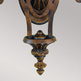 The Drawing-1 Room 2 Light Wall Light in Walnut showcases an ornate, bronze-colored metal scrollwork design with intricate detailing and a pointed finial in the Edwardian style. Its craftsmanship displays classic, elegant curves and carved embellishments, all set against a neutral background with a subtle walnut finish.