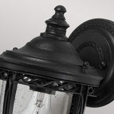 Close-up of the English Bridle 1 Light Outdoor Small Wall Lantern in a black finish, showcasing its vintage-inspired design with ornate detailing and a clear glass shade that reveals the lightbulb inside, set against a simple light gray background.