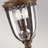 The English Bridle 3 Light Outdoor Medium Pillar Lantern in bronze boasts a vintage design with three candle-shaped lights housed inside a clear seeded glass enclosure. Its detailed metalwork and rustic charm lend an elegant touch.