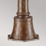 Here's a revised sentence incorporating the product data:

Close-up of the English Bridle 3 Light Outdoor Medium Pillar Lantern - Bronze, showcasing its bronze-colored metal base with a flared, textured design. The cylindrical base gracefully tapers upwards and is secured with small bolts, while clear seeded glass enhances the piece against a simple light gray background.