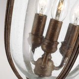 A close-up view of the English Bridle 3 Light Outdoor Large Chain Lantern showcases its vintage style with three exposed bulbs housed within a clear, slightly textured glass shade. The fixture's British Bronze Finish imparts an antique appearance, making it ideal for elegant outdoor lighting.