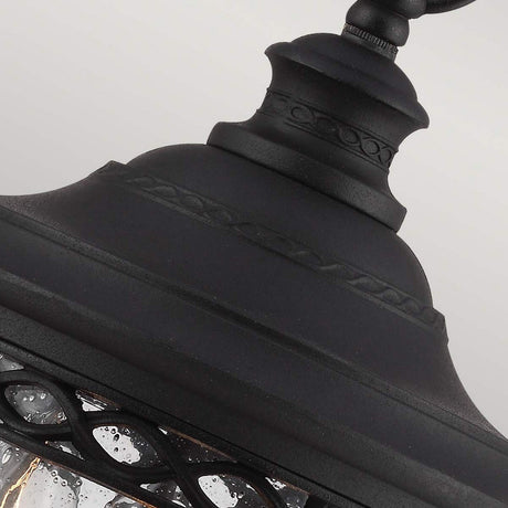 A detailed view of the English Bridle 3 Light Outdoor Medium Chain Lantern - Black showcases its vintage flair. This outdoor lighting fixture features a decorative top and a metal frame with intricate patterns, while its textured bubbled glass elevates its elegant design, adding timeless charm to any setting.