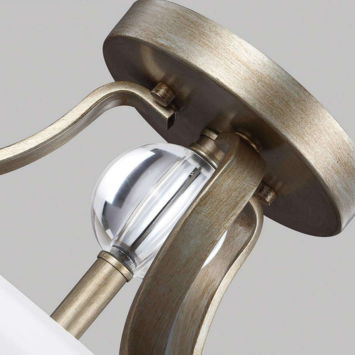 Close-up of the Evington 2 Light Semi Flush fixture, showcasing a modern design with a sunset gold finish. It features a brushed metal frame supporting a clear round glass orb in the center, with elegantly curved metal supports connecting to the ceiling mount.