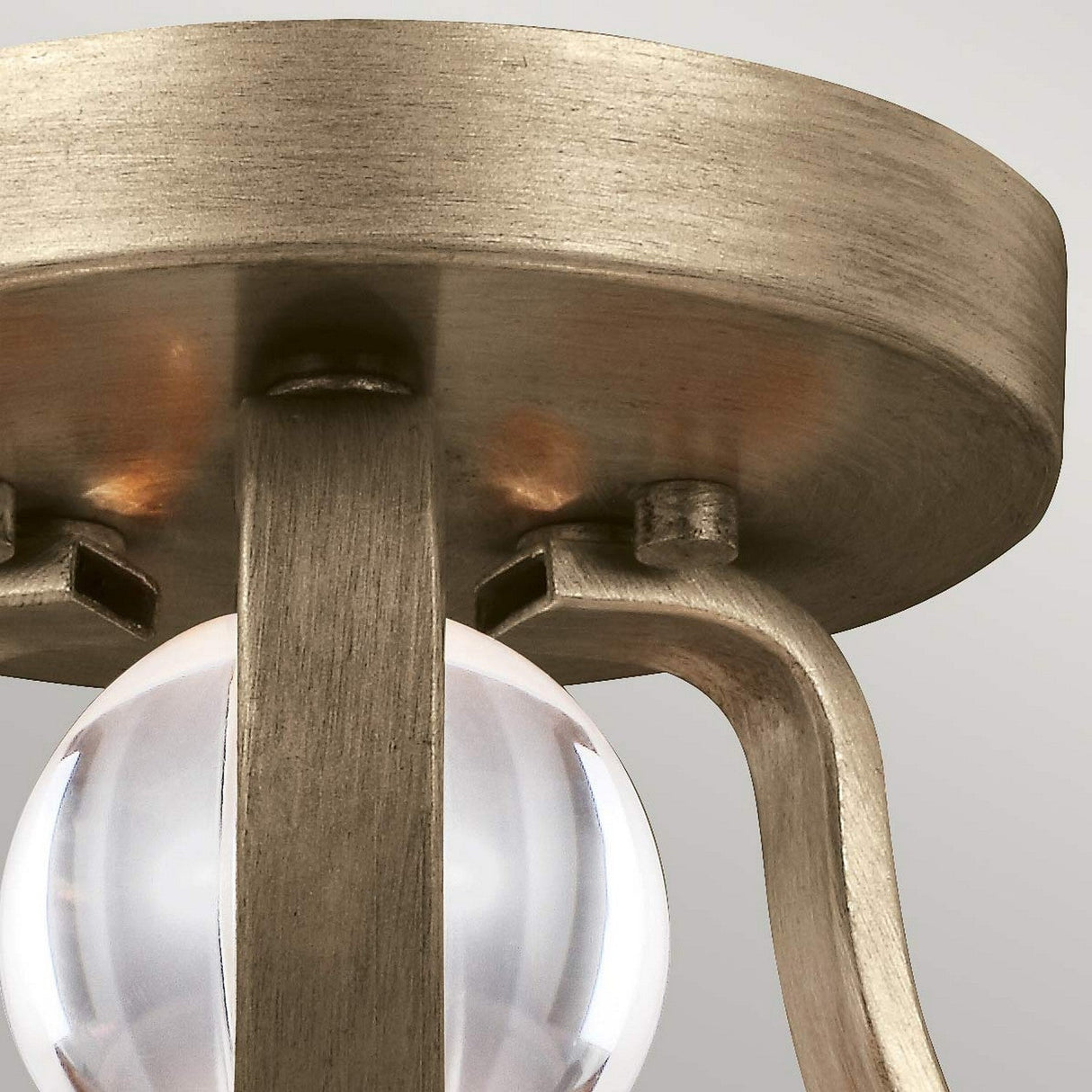 A close-up of the Evington 2 Light Semi Flush - Gold highlights its metallic design with a brushed finish. It showcases a timeless style with a clear spherical glass element hanging gracefully, set against a plain light gray background that accentuates its elegance.