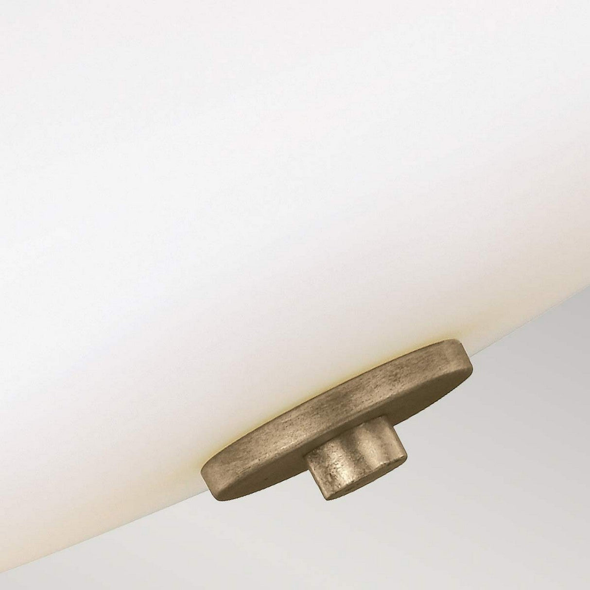 A detailed view of the Evington 2 Light Semi Flush in gold showcases a circular metallic fastener in a sunset gold finish, which secures a frosted glass shade. The fastener is centrally positioned at the bottom, offering an elegant contrast to the sleek, white surface of the blown opal etched glass.