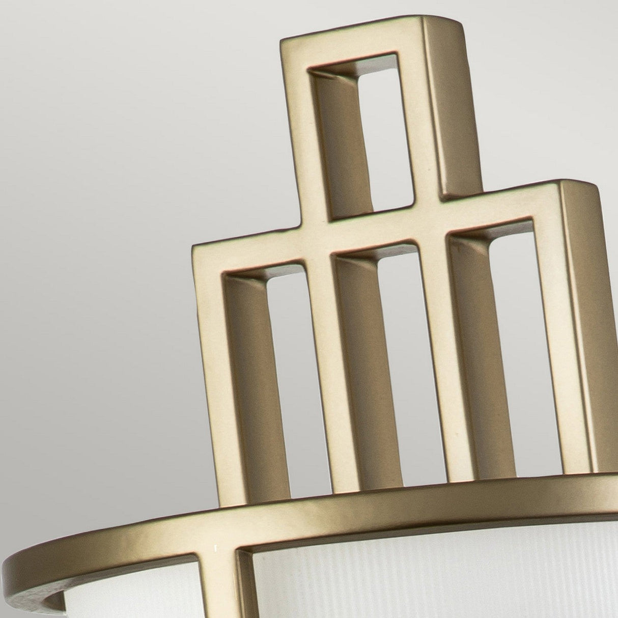 A detailed view of the Fusion 1 Light Wall Light - Painted Natural Brass highlights its geometric design, featuring intersecting vertical and horizontal metal bars. The painted natural brass finish underscores its metallic appeal, complemented by the ribbed opal glass shade that enhances its contemporary elegance against a neutral backdrop.