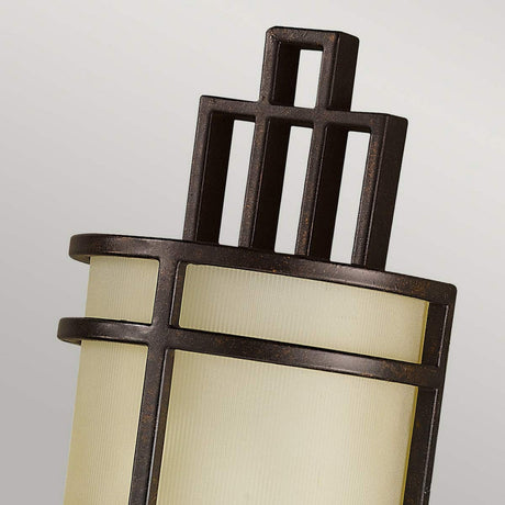 Close-up of the Fusion 1 Light Wall Light in Grecian Bronze. The design features a vertical ribbed glass shade with a dark metal frame and a geometric pattern on top, creating a sophisticated and elegant look reminiscent of Arts & Crafts styling.