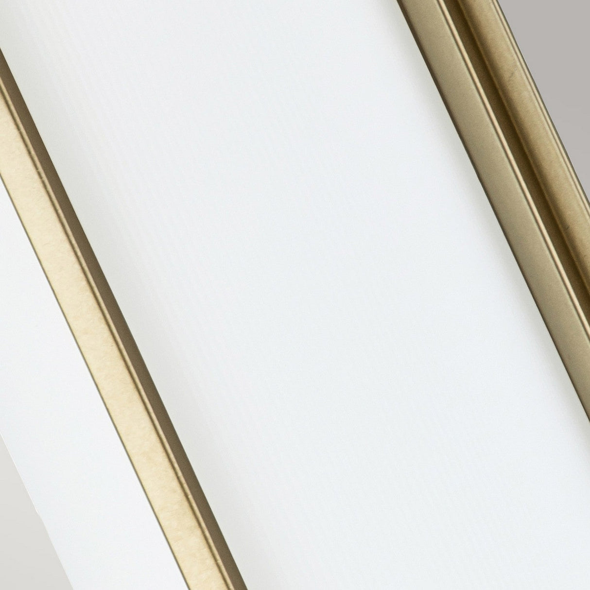 A close-up view showcases two parallel light beige frames or borders set against a white background, echoing the elegance of the Fusion 2 Wall Light in Painted Natural Brass. These frames intersect diagonally from the top left to the bottom right corner of the image.