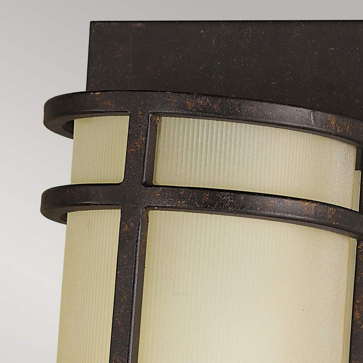 Close-up of the Fusion 2 Light Wall Light - Grecian Bronze, a wall-mounted outdoor fixture showcasing a Grecian Bronze frame and frosted glass panels. The design highlights curved lines intersecting at right angles, contributing to its modern and sleek look.