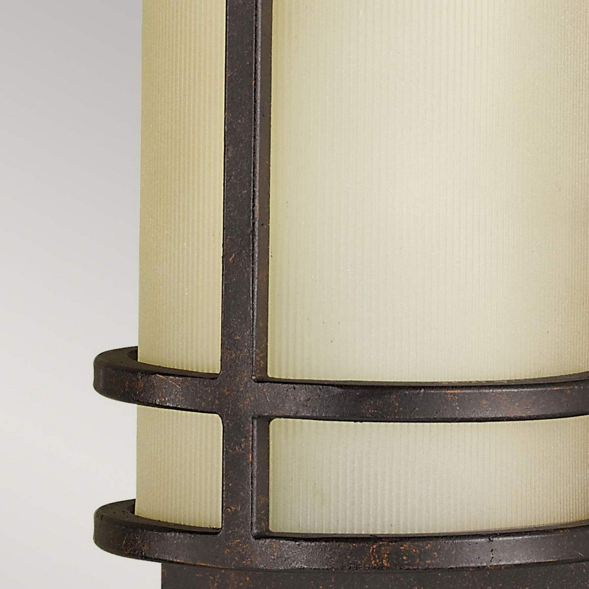 Close-up of the Fusion 2 Light Wall Light - Grecian Bronze, showcasing its amber glass shades and distinctive frame with vertical and horizontal bars, set against a light gray background.