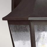 Close-up of the Galena 1 Light Outdoor Medium Wall Lantern in a vintage style, featuring a sable-colored dark metal frame and seeded glass panels. The glass is adorned with rain droplets, partially illuminating the lantern to cast a warm glow.