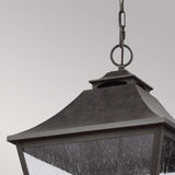 In a close-up shot, the Galena 4 Light Outdoor Chain Lantern - Grey hangs elegantly from a chain. This dark, metal lantern features a classic square design with clear seeded glass panels that stands out against the muted gray background. Its traditional style makes it an elegant IP44 rated fixture suitable for any setting.