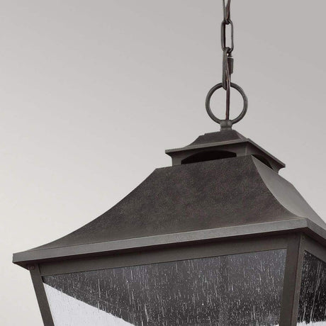 In a close-up shot, the Galena 4 Light Outdoor Chain Lantern - Grey hangs elegantly from a chain. This dark, metal lantern features a classic square design with clear seeded glass panels that stands out against the muted gray background. Its traditional style makes it an elegant IP44 rated fixture suitable for any setting.