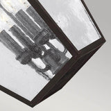 Close-up of the Galena 4 Light Outdoor Chain Lantern, featuring a geometric design with glass panes and a metal frame. Visible bulbs shine through the seeded glass, exuding a modern industrial vibe. Perfectly suited for any setting, its backdrop is a plain, muted gray.