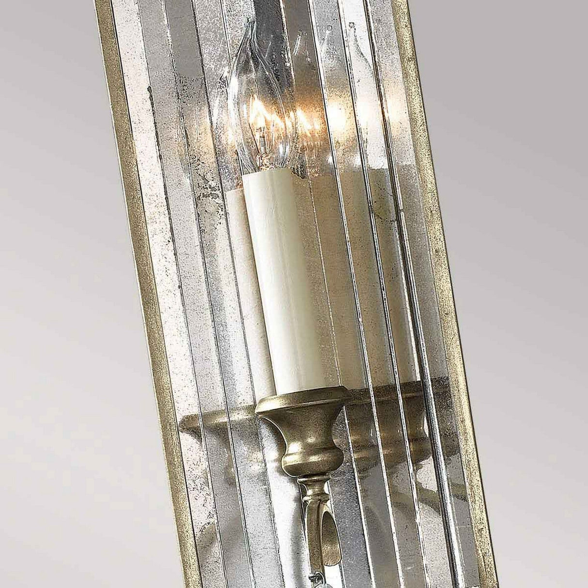 Close-up of the Gianna 1 Light Wall Light, featuring a candle-like bulb encased in ribbed, reflective glass. Its gilded silver finish adds a classic and elegant touch to the design, exuding a vintage charm reminiscent of Italian interiors.