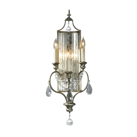 The Gianna 3 Light Wall Light - Gilded Silver exudes a vintage charm with its elaborate metal frame and two candle-shaped lights. The hand-cut crystals embellishing it enhance the shimmering glow against a distressed mirrored panel.