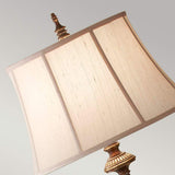 A close-up of the Gibson 1 Light Floor Lamp in dark brown, featuring a square desert linen fabric shade and a decorative antique-style brass base set against a neutral background.