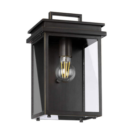 The Glenview 1 Light Outdoor Medium Wall Lantern in antique bronze features a black rectangular design with a clear glass enclosure and vintage-style exposed filament bulb, showcasing its prairie-style design. The antique bronze finish enhances its modern, clean appearance against a white background.