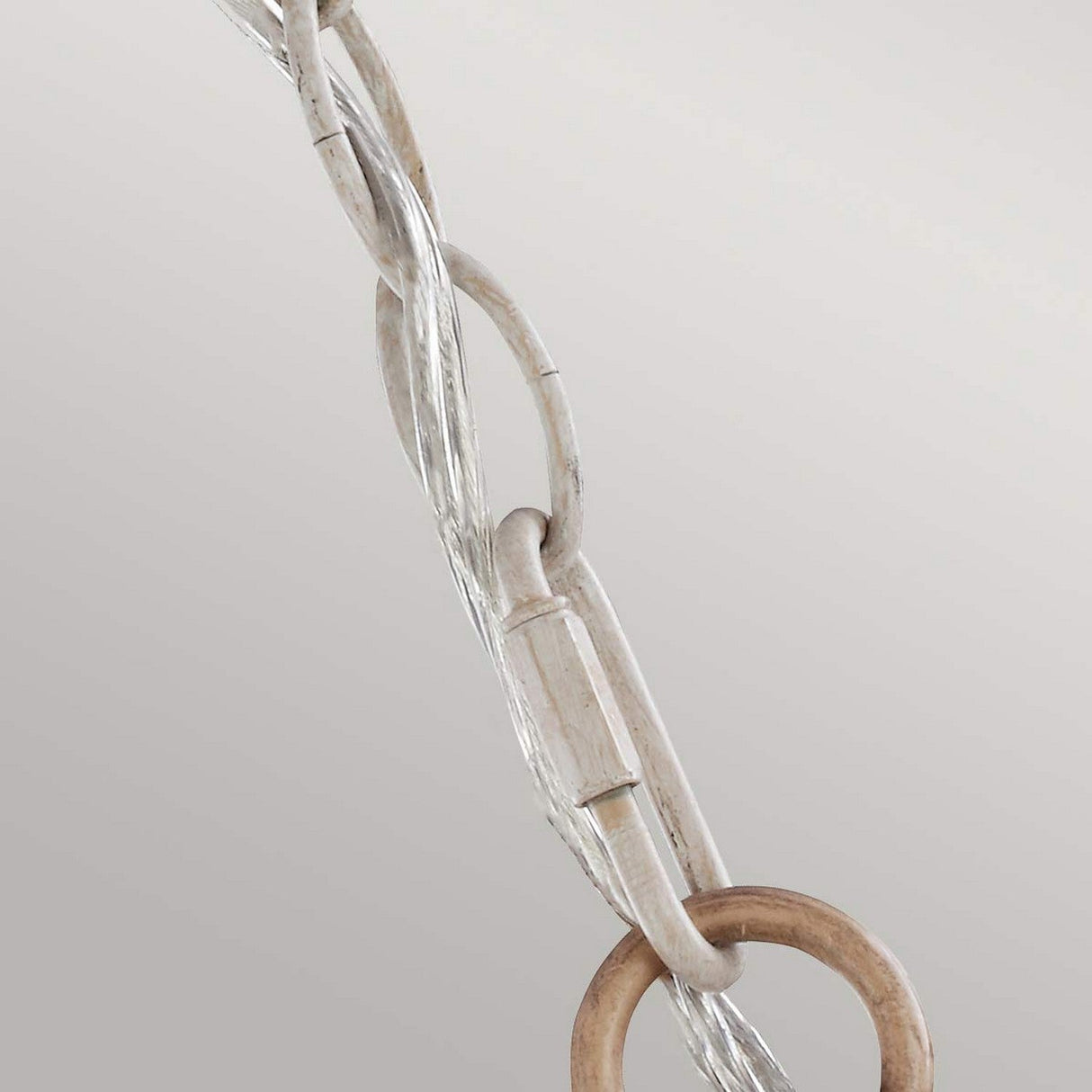 A close-up of the Hartsville 3 Light Chandelier in Chalk Washed/Beachwood showcases a twisted metal cable with a wooden ring and two metal links, capturing the charm of rustic design against a neutral backdrop. Ideal for adding a coastal casual touch or enhancing your distinctive chandelier accents.