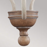 Close-up of the Hartsville 3 Light Chandelier in a Chalk Washed/Beachwood finish, showcasing a wooden finial with a smooth, rounded shape, ideal for rustic design. The layered detailing is attached to curving wooden elements above, resembling those in coastal casual spaces. A neutral gray backdrop enhances its understated elegance.