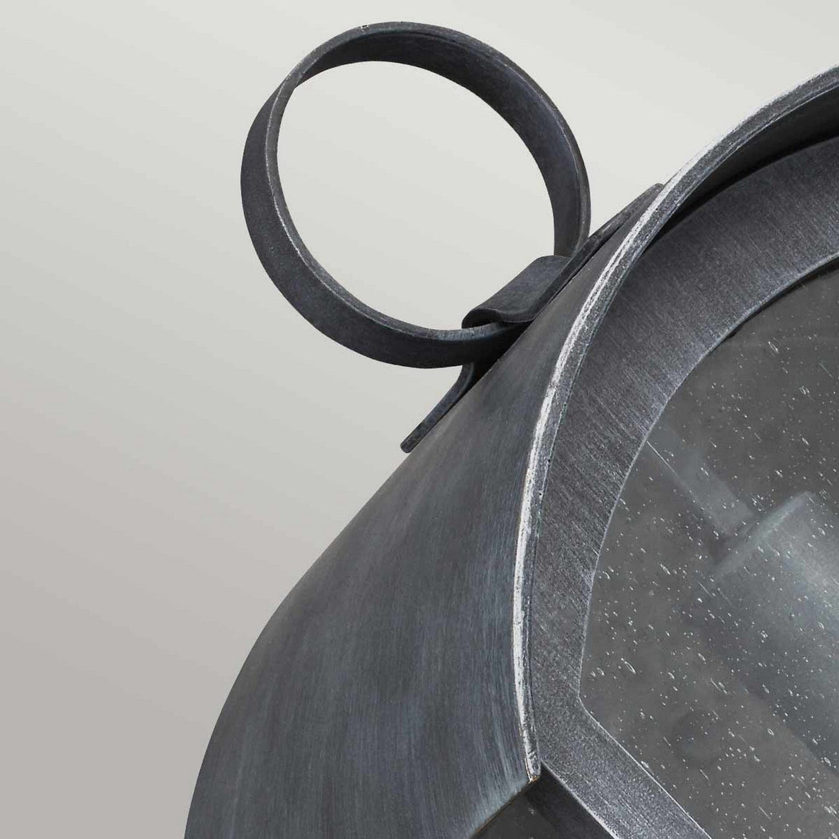 A close-up view of the Hodges Outdoor Large Wall Lantern in Ash Black showcases its metallic, industrial-style design featuring a curved handle and a glass panel. Its weathered ash black finish enhances its rustic charm, making it an ideal complement to farmhouse aesthetics against a neutral background.